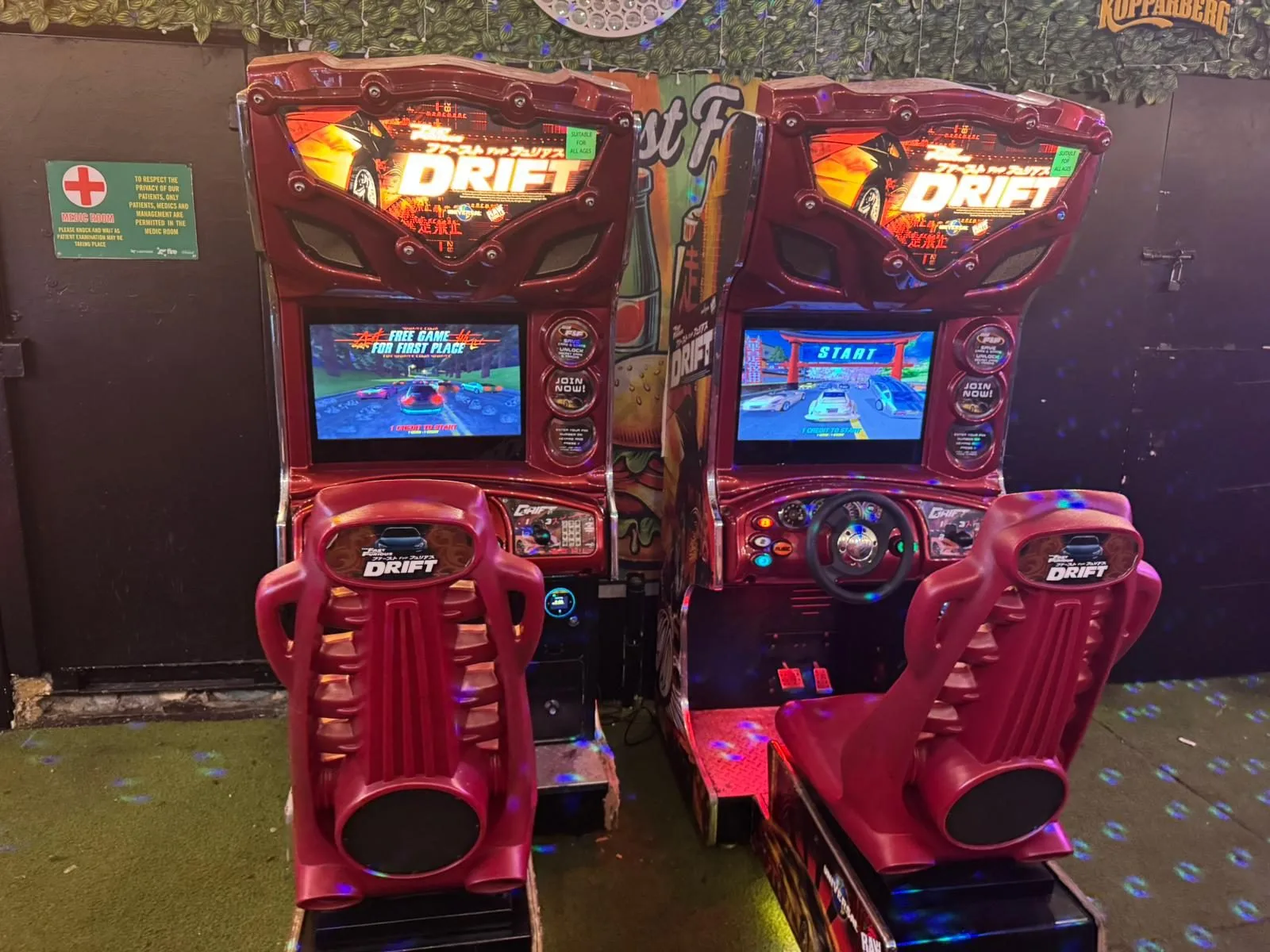 Two red DRIFT-branded twin sit-down racing simulators side by side